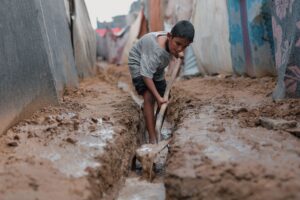 child in gaza camp working in muddy conditions