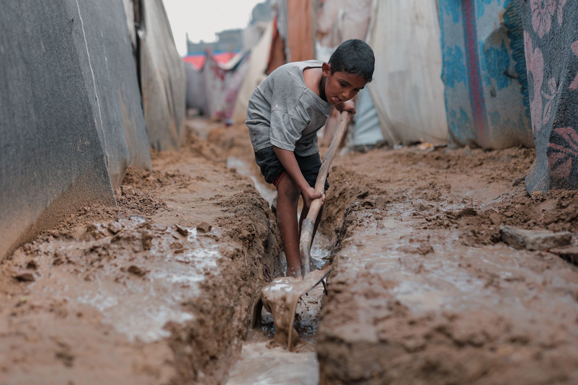 child in gaza camp working in muddy conditions
